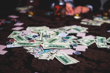 Poker masası, bir deste kart, jeton, alkol, dolar parası ve poker oynayan zengin insanlar.