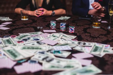 Poker masası, bir deste kart, jeton, alkol, dolar parası ve poker oynayan zengin insanlar.