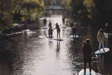 Bir grup sup sörfçüsü ayağa kalkar, kadınlar şehrin nehri ve kanalında yazın güneşli havalarda birlikte kürek çeker.