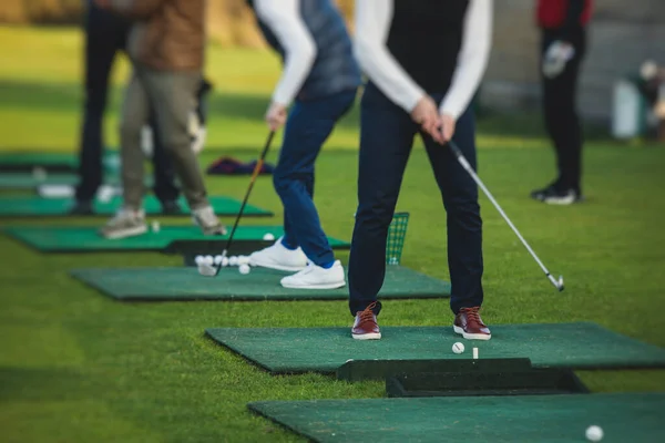 Group of golfers practicing and training golf swing on driving range practice, men playing on golf course, golf ball at golfing complex club resort, summer sunny da