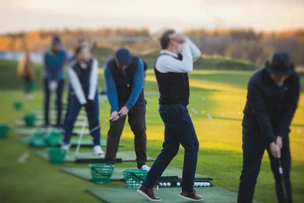 Group of golfers practicing and training golf swing on driving range practice, men playing on golf course, golf ball at golfing complex club resort, summer sunny da