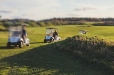 Golf elektrikli arabaları gün içinde golf sahasında, golf arabaları tatil köyünde golfçülerle sürüyor.