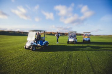Golf elektrikli arabaları gün içinde golf sahasında, golf arabaları tatil köyünde golfçülerle sürüyor.