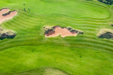 Kırsal alandaki golf sahasının canlı hava aracı manzarası, zengin yeşil bir çim ve kum sığınakları olan arazi yaz güneşli bir gün, bir grup golfçü yürüyüş ve oyun, golf kulübü müsabakaları