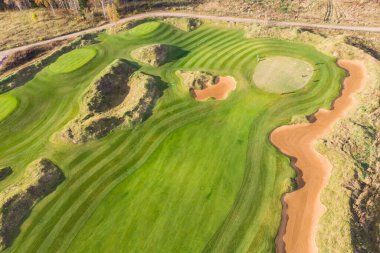 Kırsal alandaki golf sahasının canlı hava aracı manzarası, zengin yeşil bir çim ve kum sığınakları olan arazi yaz güneşli bir gün, bir grup golfçü yürüyüş ve oyun, golf kulübü müsabakaları