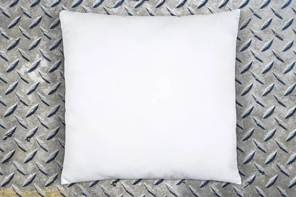 Square white throw pillow resting atop a weathered metal diamond plate background