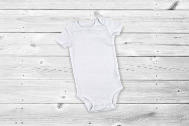 Gri yıpranmış ahşap arka planda dinlenen beyaz bebek tulumu..