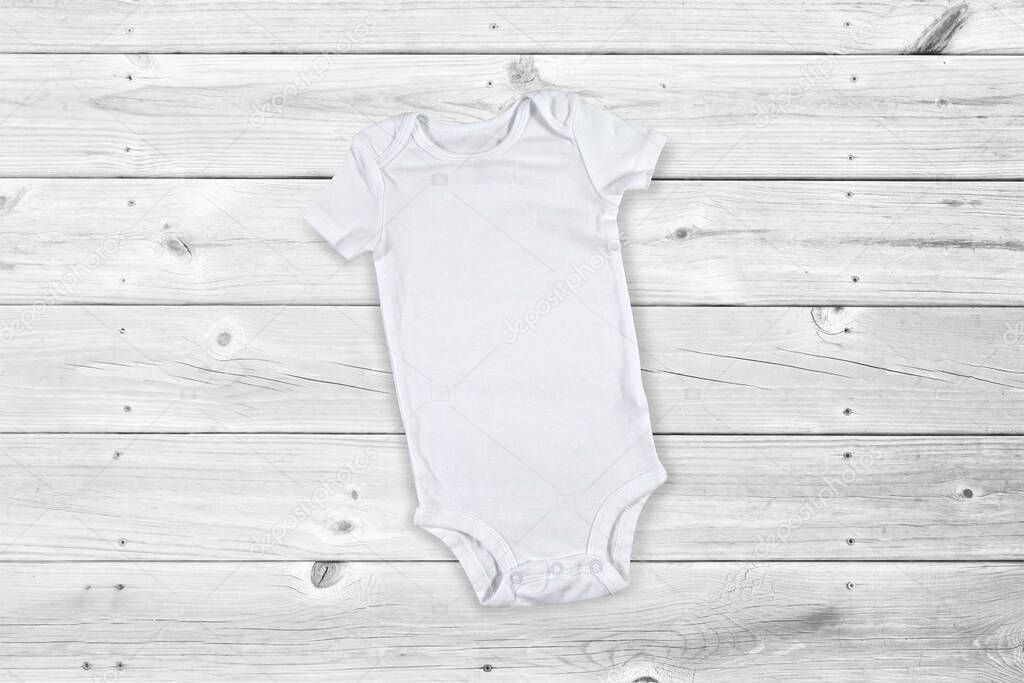 White baby bodysuit resting on a gray weathered wood background.
