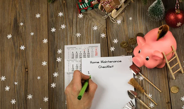 Sheet of paper  with Home Maintenance Checklist. Pink piggy bank on a new year\'s background. Top view