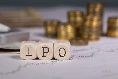 Abbreviation IPO composed of wooden letter. Stacks of coins in the background. Closeup clipart