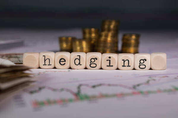 Word HEDGING composed of wooden letter. Stacks of coins in the background. Closeup