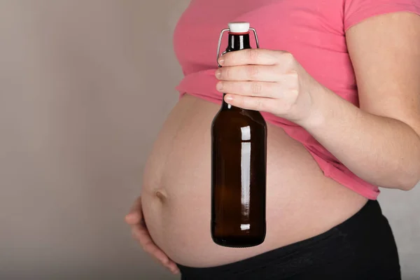 Jovem grávida mantém garrafa de vidro de cerveja perto de seu bel — Fotografia de Stock