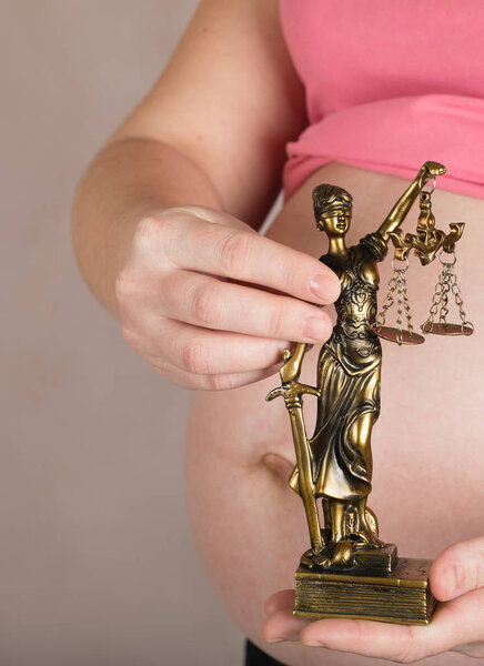 Young pregnant woman keeps statue of Themis. 