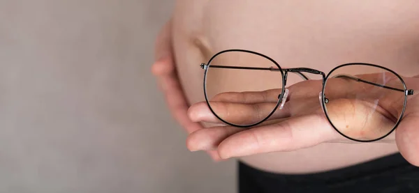 Jovem grávida mantém óculos de olho na frente de sua barriga . — Fotografia de Stock
