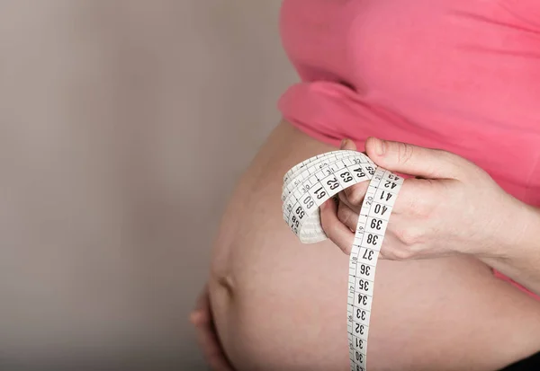 Молодая беременная женщина держит измерительную ленту перед своим звонком — стоковое фото