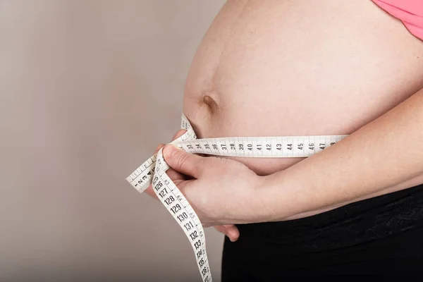Молодая беременная женщина измеряет свой живот с помощью измерительной ленты . — стоковое фото