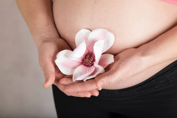 Молодая беременная женщина держит искусственный цветок орхидеи рядом с ней — стоковое фото
