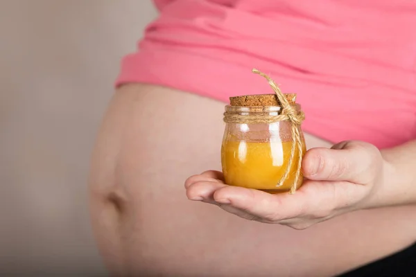 Young pregnant woman keeps glass bottle of natural honey. — Stock Photo, Image