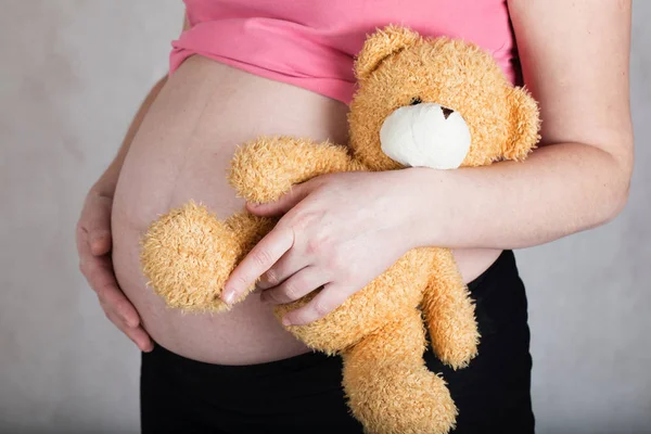 Junge schwangere Frau hält braunen Plüsch-Teddy. Stockbild