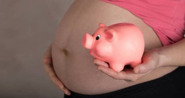 Genç hamile kadın pembe kumbara tutar. 