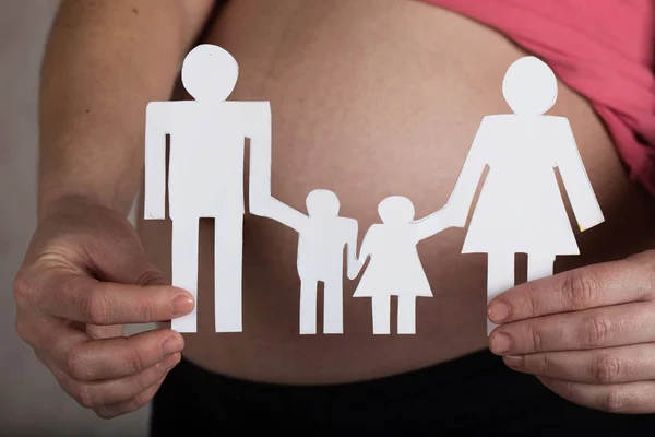 Young pregnant woman keeps paper cutouts of a family. Closeup — Stock Photo, Image