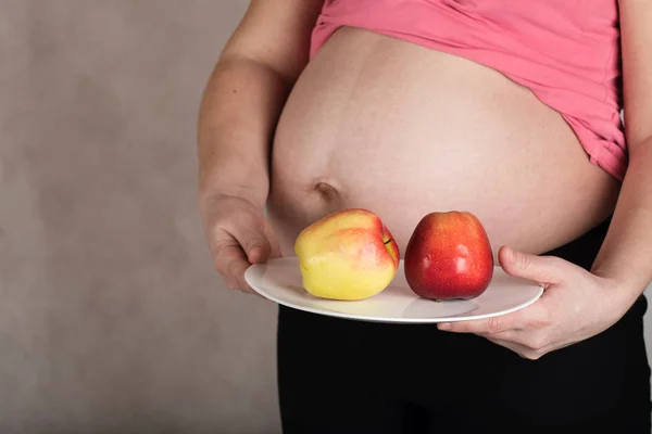 Молодая беременная женщина держит белую тарелку с красными яблоками на ней . — стоковое фото