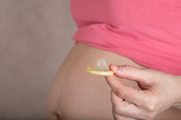 Молодая беременная женщина держит презерватив близко к животу
. 