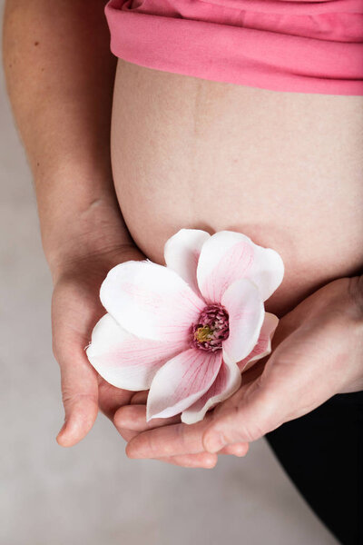 Young pregnant woman keeps artificial orchid flower close to her