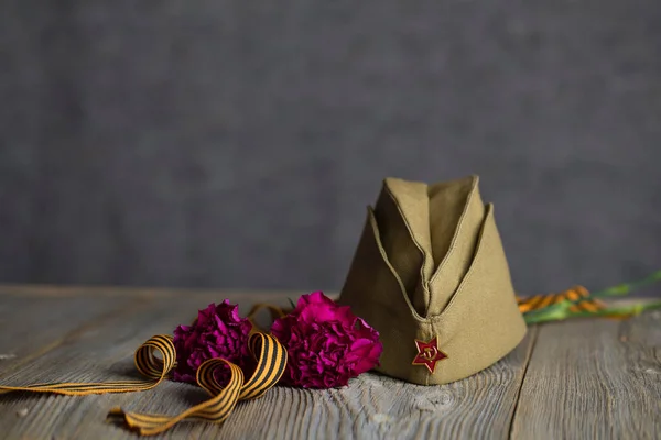 Gorra militar, claveles, cinta de San Jorge sobre un surfac de madera —  Fotos de Stock