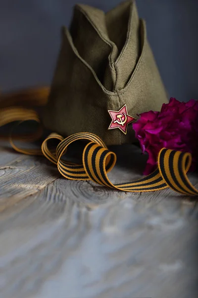 Boné militar, cravos, fita de São Jorge em uma sobremesa de madeira — Fotografia de Stock