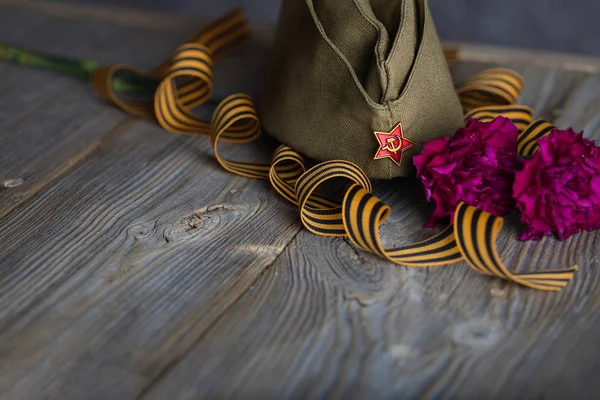 Военная шапка, гвоздики, Георгиевская лента на деревянном карнизе — стоковое фото