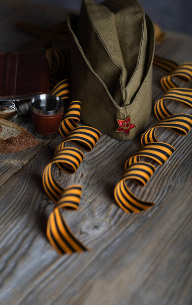 Military cap, carnations, Saint George ribbons, flask with alcoh