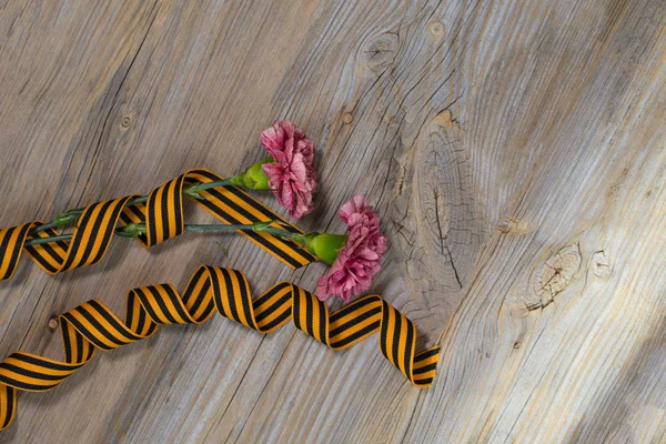 Two pink carnations, Saint George ribbon on a wooden surface. — Stock Photo, Image