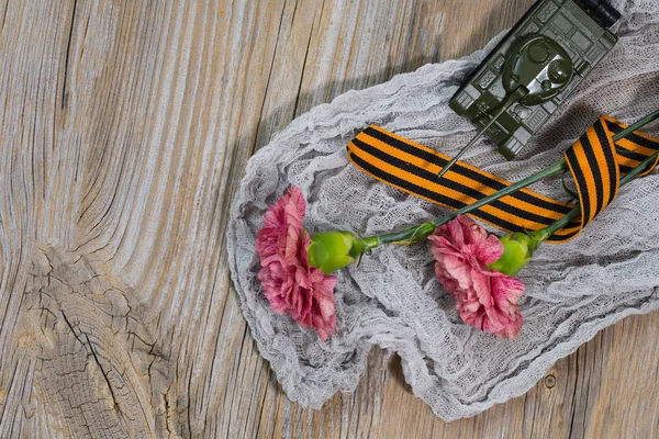 Zwei rosa Nelken, Saint George Band und Militärpanzer auf einer Holzoberfläche. — Stockfoto