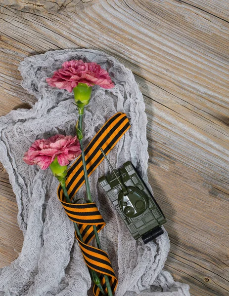 Two pink carnations, Saint George ribbon and military tank on a — Stock Photo, Image