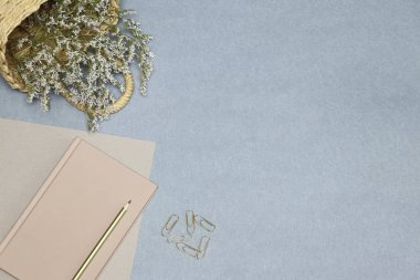 Pembe Notebook, kağıt klipler, mavi masada çiçekler ile saman sepeti
