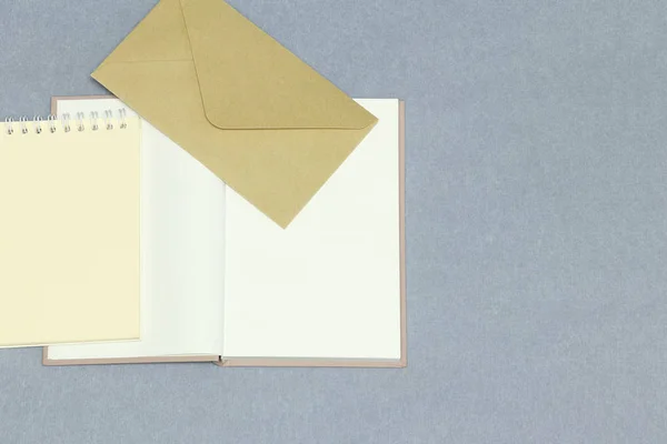 The opened notebook, yellow paper, envelope on the grey background