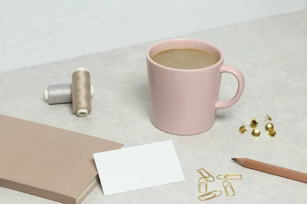 The mockup business card,  pink book, golden pencil, paper clips, pins and threads, cup of coffee  on granite texture
