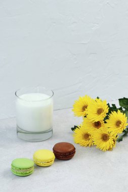 Gri beton masada bir bardak süt, makaron ve sarı çiçek