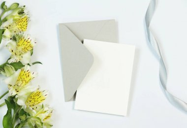 Çiçekler, zarf ve kurdele ile beyaz arka plan üzerinde mockup davetiye