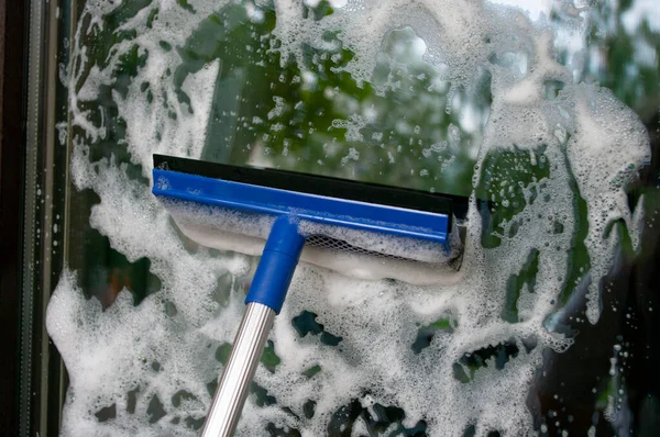 Cleaning glass of window using a squilgee with detergent foam. Housekeeping concept.