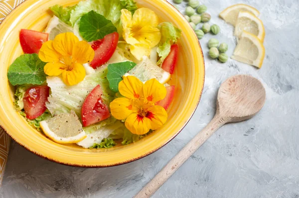 Sarı seramik kasede nasturtiyum çiçekli, domatesli ve limonlu taze yaz salatası..