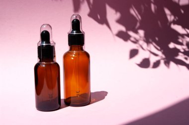 Doğal kozmetik yağı için cam damlası. Pembe arkaplan, gölgeden çıkıyor. Boşluğu metin için kopyala. Organik ürün. Vücut bakımı.