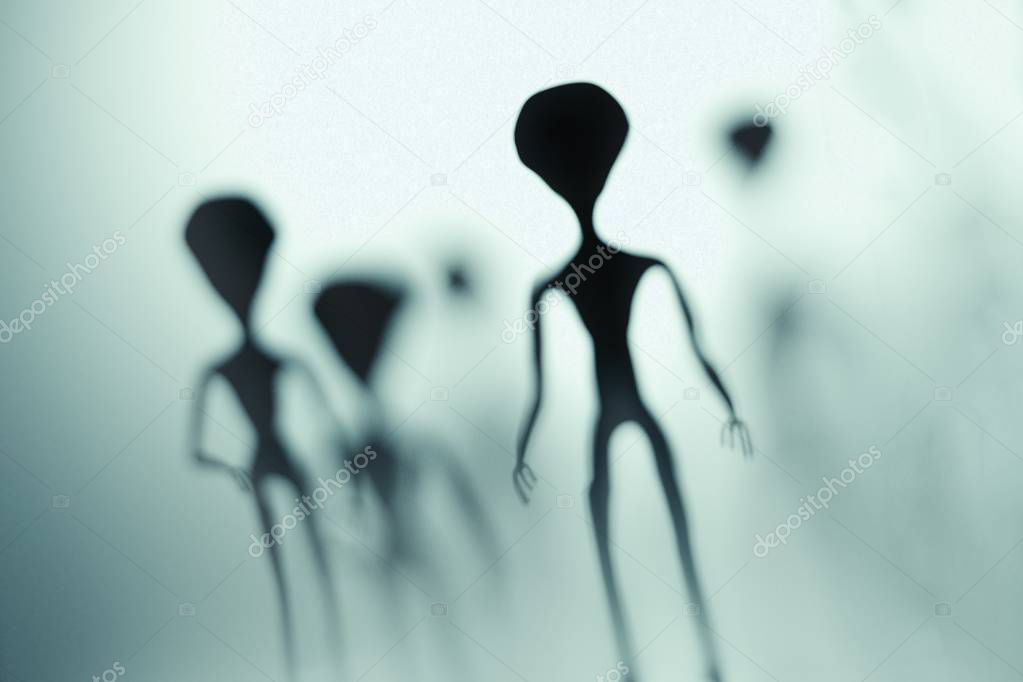 Spooky silhouettes of aliens and bright light in background. 3D rendered illustration.