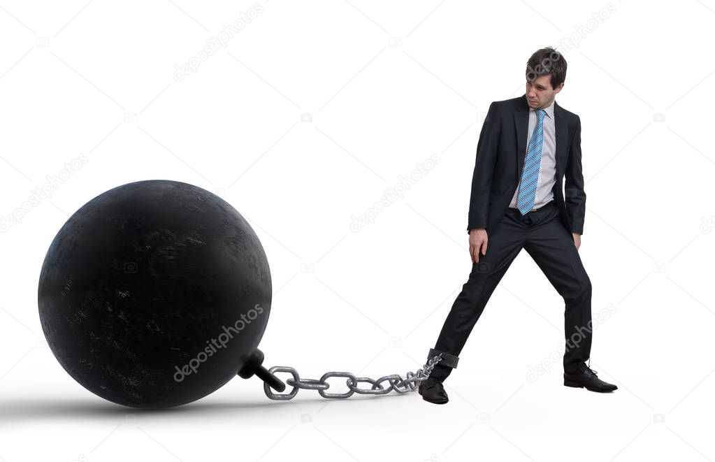 Young businessman has chained big metal ball to his leg. Isolated on white background.
