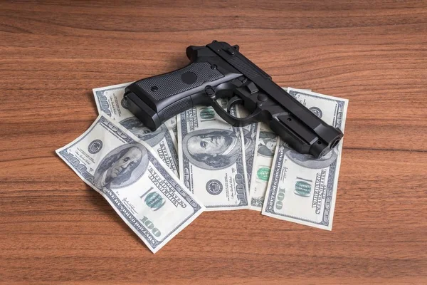 Robbery concept. Gun with money on wooden background.