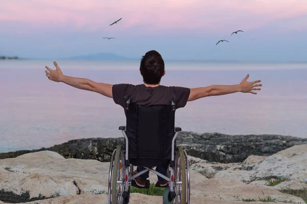 Homem com deficiência em cadeira de rodas perto da praia ao pôr do sol . — Fotografia de Stock