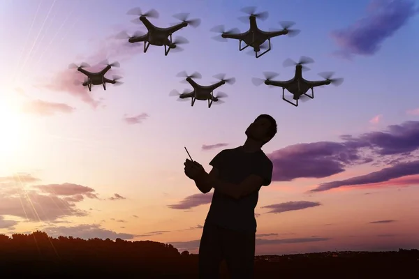 Silhouette of man controlling drones flying on sky at sunset.