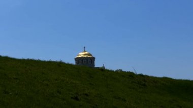 Tepenin arkasından bakmak Christian kilisenin kubbesi. Kilisenin altın kubbesi mavi gökyüzüne karşı çim görülür.