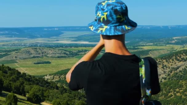 Jovem Assume Uma Câmera Ação Uma Paisagem Montanhosa Homem Chapéu — Vídeo de Stock